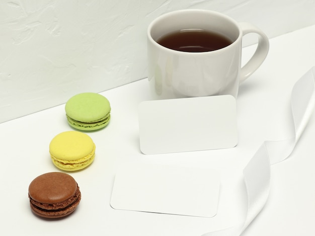 Paper cards on white background with macaron, ribbon and cup of coffee