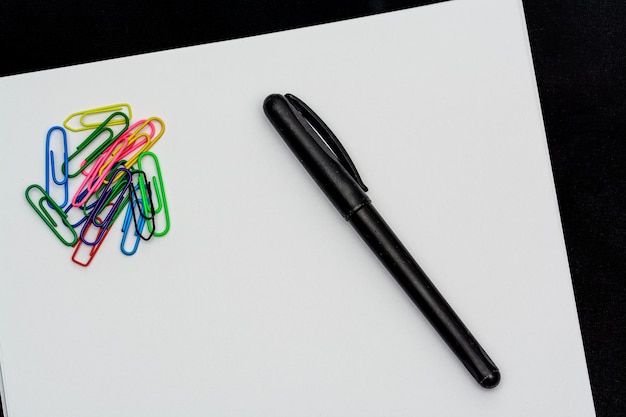 Скрепка и ручка на белом листе с черным фоном