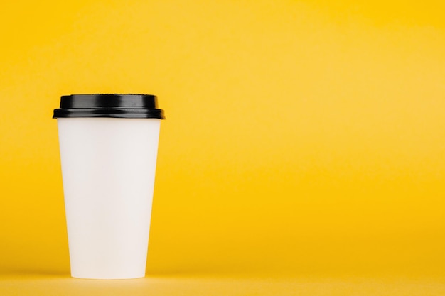 Paper coffee container with black lid on yellow background