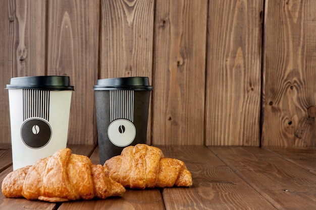 Фото Бумажная чашка кофе и круассаны на деревянном фоне