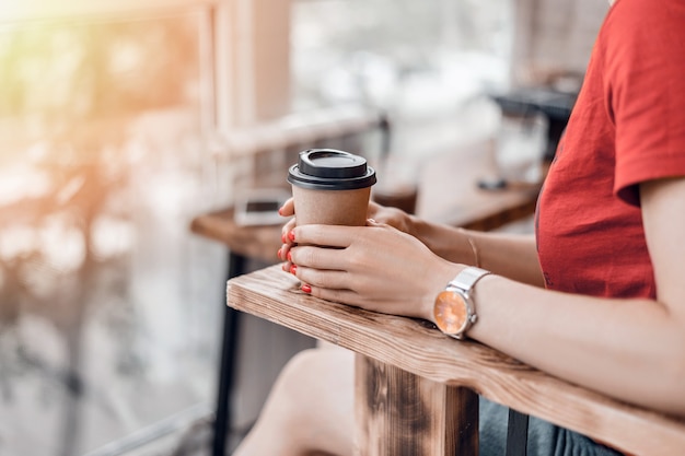 Foto tazza di caffè di carta per andare nelle mani della donna con il manicure rosso mentre era seduto nel caffè.