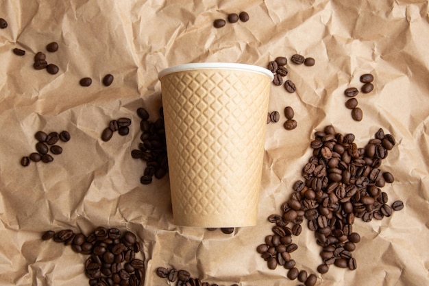 Paper coffee cup studded with coffee beans on the background of kraft paper