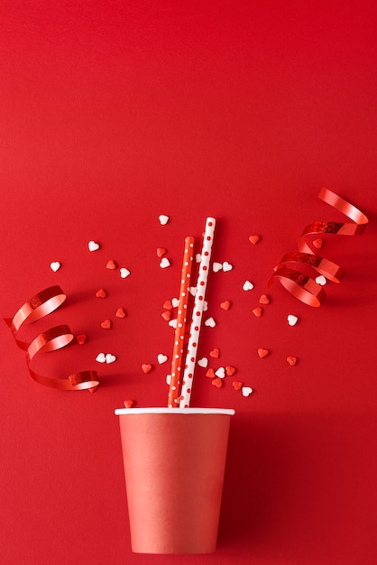 Paper coffee cup with festive decorations and confetti on red backgrond, top view flat lay. Creative minimalism concept