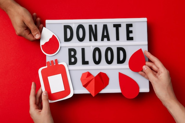 Paper container of blood in hand with red heart on red background Blood donation