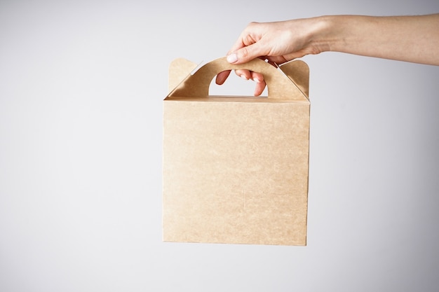 Paper craft bag, eco packaging in a female hand on a gray\
background.