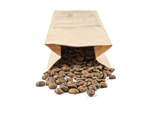 Paper craft bag lies with roasted coffee beans spilled out of it isolated on white surface