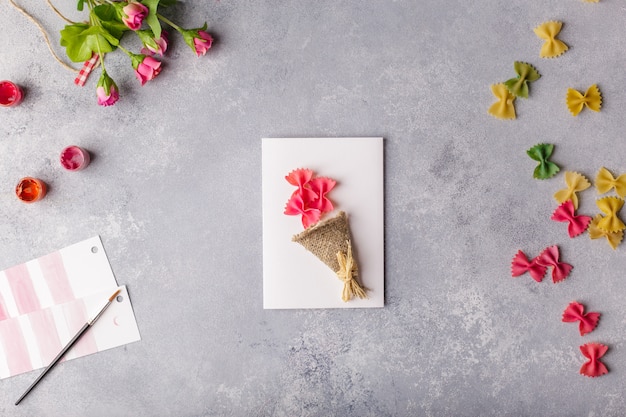 Paper crafts for mother day, 8 march or birthday. Small child doing a bouquet of flowers out of colored paper and colored pasta.