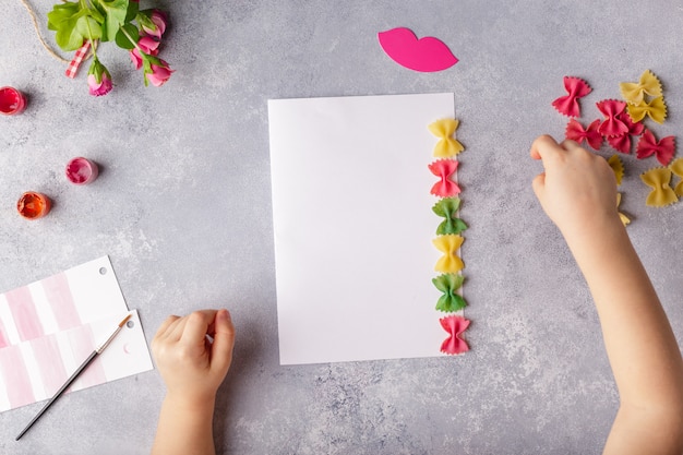 Paper crafts for mother day, 8 march or birthday. Small child doing a bouquet of flowers out of colored paper and colored pasta.