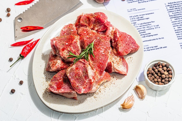 豚肉を準備するための紙の料理レシピ原材料には、豚ロース片のスパイスとハーブが含まれます準備健康食品のコンセプトハードライト暗い影白い背景の接写