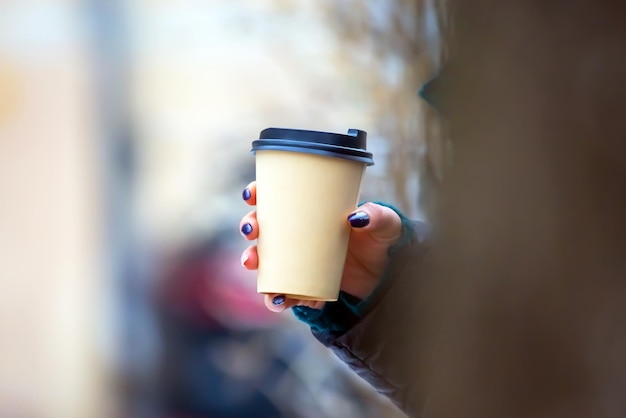 Paper cup of coffee in a woman hand on the street