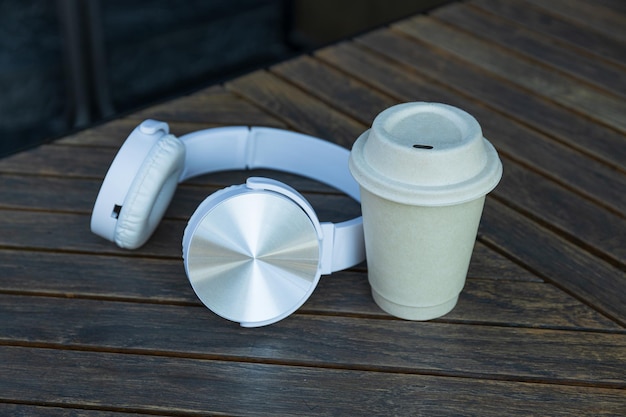 Paper cup and headphones on wooden table outdoors