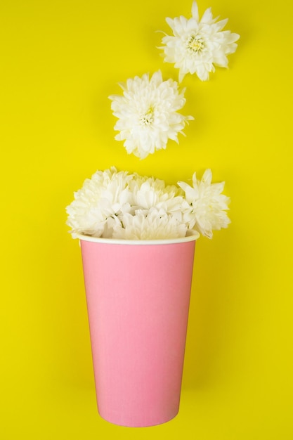 黄色の背景にピンク色の持ち帰り用のコーヒー用の紙コップが横たわっています 白い花が横たわっています