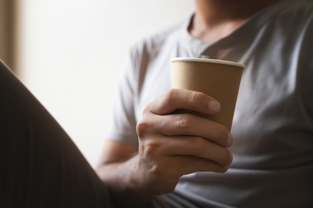 Paper cup with coffee in hand at the man in the room