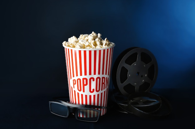 Paper cup with tasty popcorn, glasses and movie reel