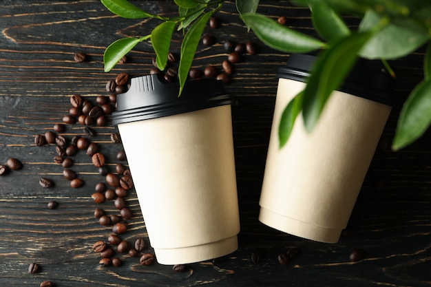 Paper cups, coffee beans and plant on wooden