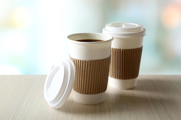 Paper cups of coffee on table on bright background