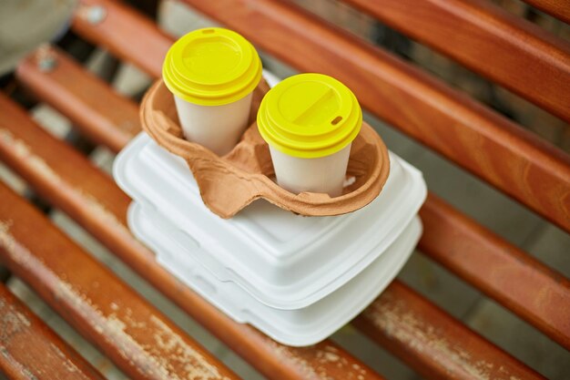 Paper cups with coffee and fast food boxes to go on a park bench outdoor takeaway food concept