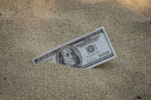 Photo paper currency 100 dollar bills partially buried in the sand