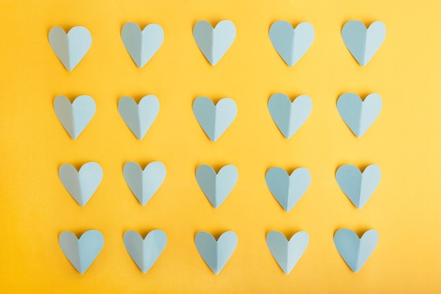 Paper cut of blue hearts in rows on yellow paper background