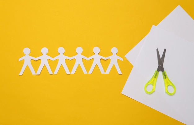 Paper cut chain of people with scissors on yellow background