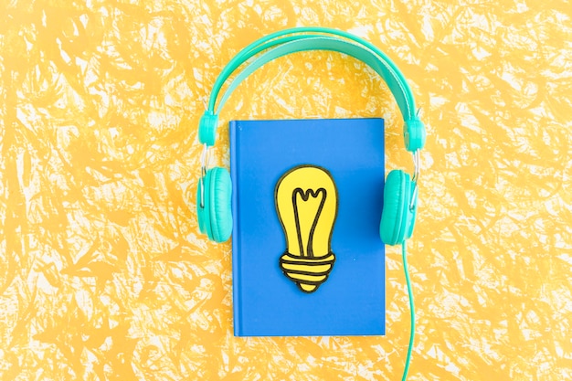 Photo paper cut out yellow light bulb on closed notebook with headphone on textured background