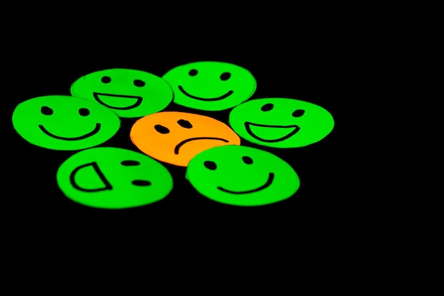 Paper cutout image of green smiley faces surrounding a sad face concept of psychology therapy emotions mental health circles of trust friendship and family Black background Selective focus