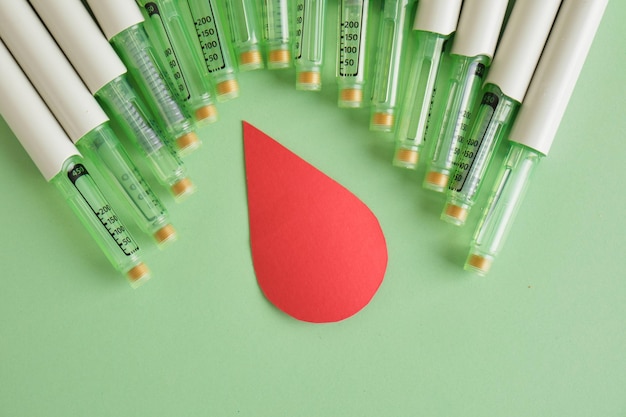 A paper drop of blood and a lot of syringe pens with insulin on a green background