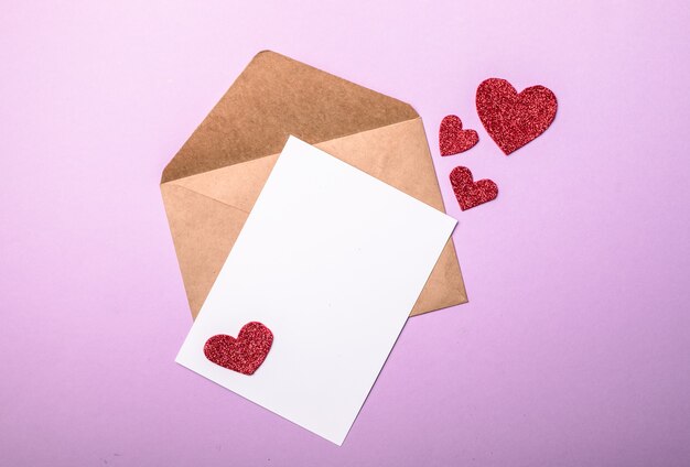 Бумажный конверт с сердечками валентинок на фиолетовом фоне. Плоская планировка, вид сверху. Романтическое любовное письмо для концепции дня святого Валентина.