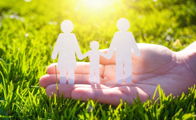 Paper family in hand on green grass background