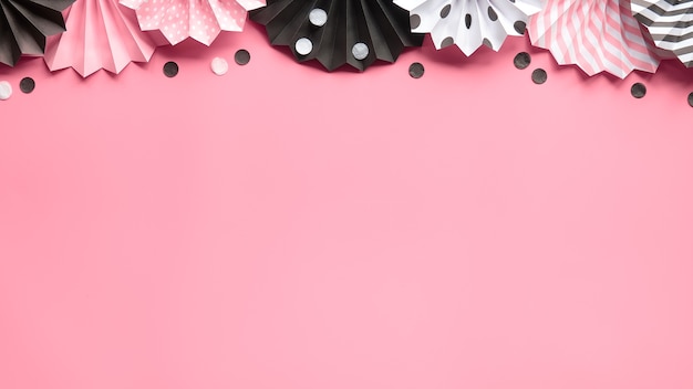 Paper fans on pink paper. Top view with copy-space. Celebration background in pink, black, white.