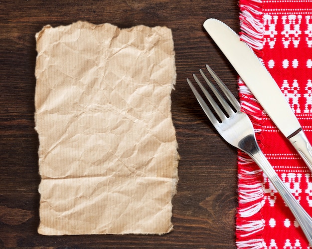 Carta, forchetta e coltello sull'asciugamano di cucina su una vista di legno del piano d'appoggio con lo spazio della copia della carta del mestiere