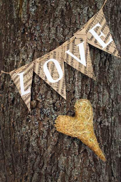 Paper garland with the inscription love, heart of hay on a tree trunk