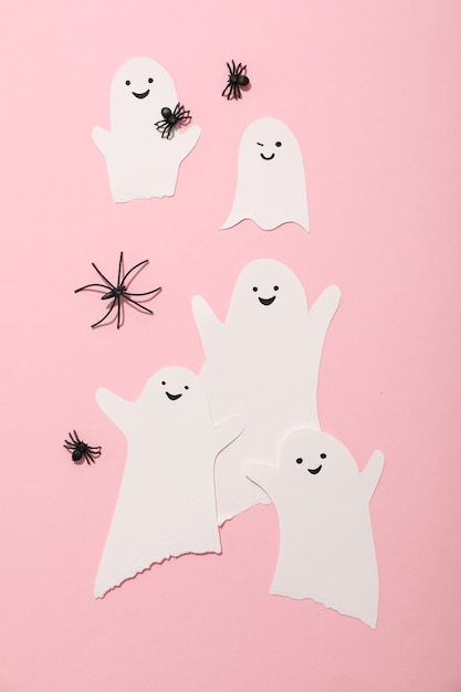 Paper ghosts and decorative spiders on pink background top view