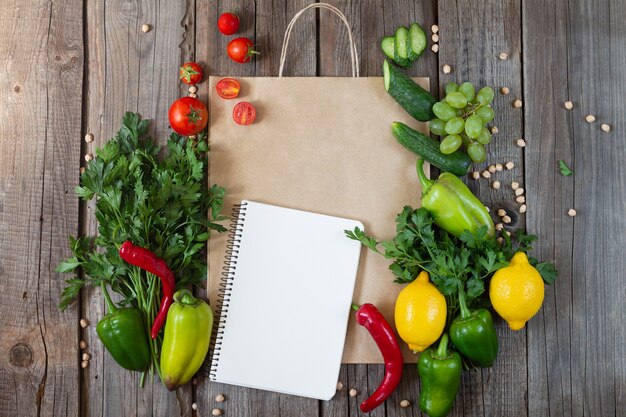 Paper grocery bag with blank notebook and fresh vegetables and fruits on wooden table