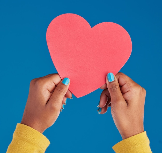Photo paper heart and hands of black woman in studio for love date and kindness invitation romance and feelings with female and shape isolated on blue background for emotion support and affectionate