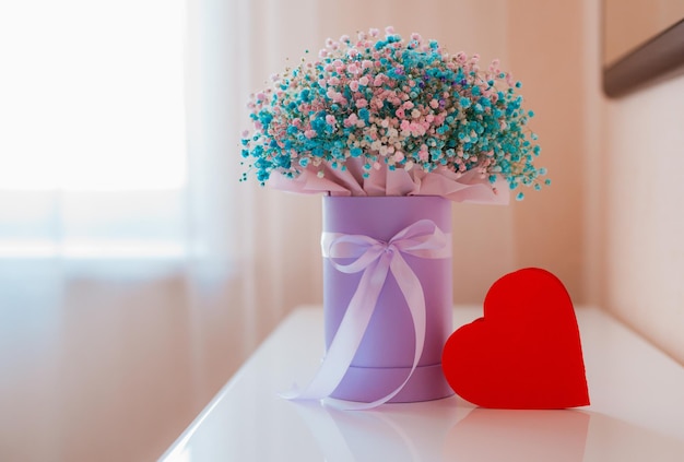 Paper heart symbol a gift box with a bouquet of colored gypsophiles on the table in the room The concept of Valentines Day Mothers Day International Womens Day March 8