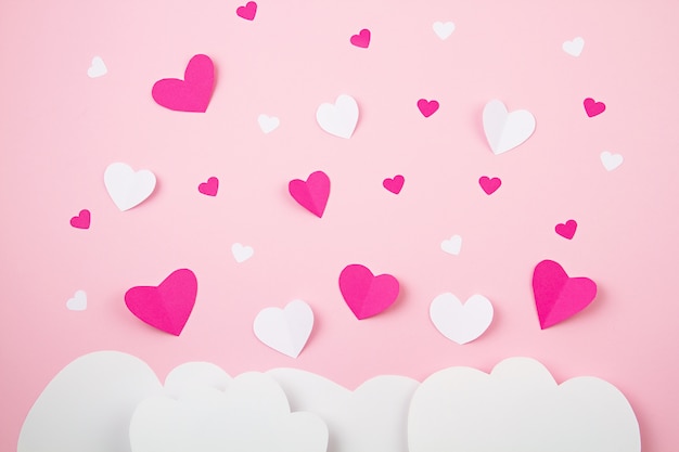 Paper hearts and clouds over pink background.