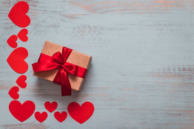 Paper hearts and a craft present with red ribbon on a light painted wooden background. Top side angle view, flat lay. Valentines day concept. Copyspace.