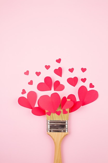 Paper hearts and paint brush over the pink pastel background