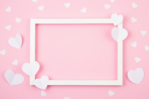 Paper hearts and white frame over the pink pastel background. 