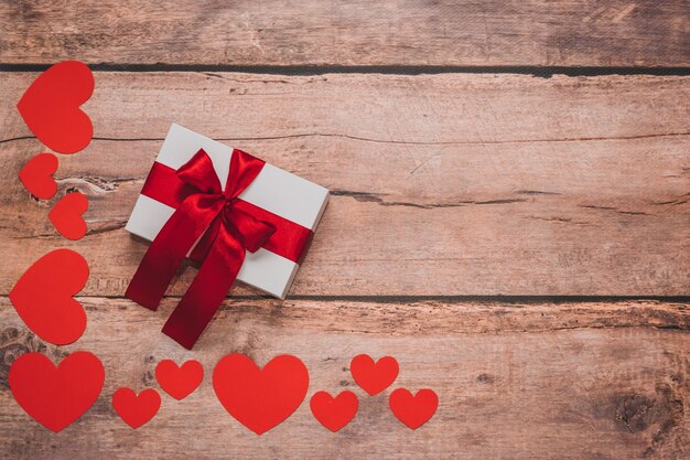 Paper hearts and a white present with red ribbon on a wooden background. Top side angle view, flat lay. Valentines day concept. Copyspace.