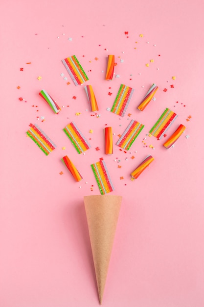 Paper horn with colorful marmalade sweets on a pink background