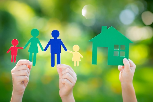 Paper house and family in hand against spring green background Real estate business concept