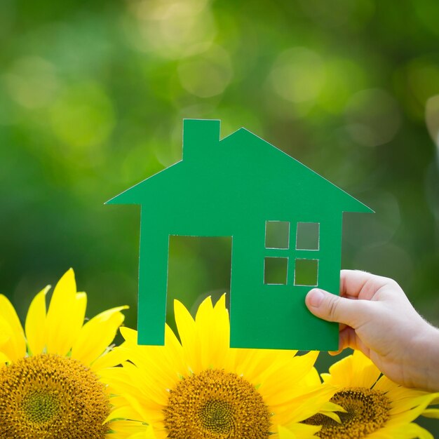 Paper house in hand against spring green background Real estate concept