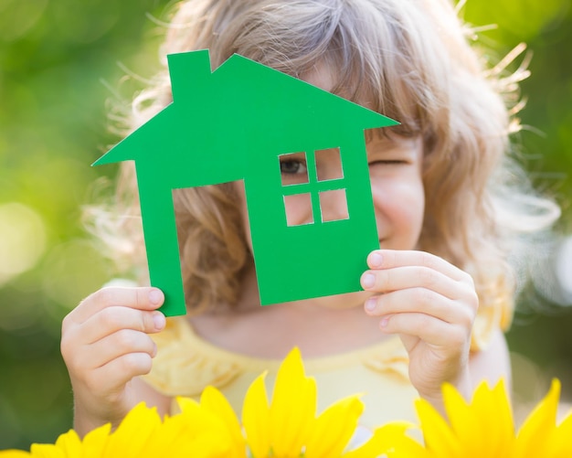 Paper house in hand against spring green background Real estate concept