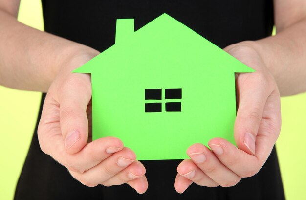 Paper house in hand on green background