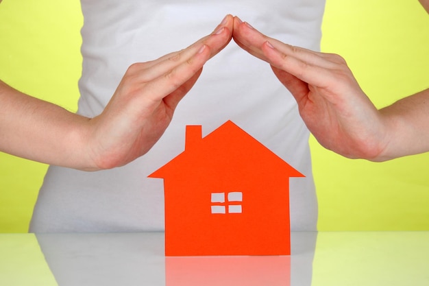 Paper house in hands on green background