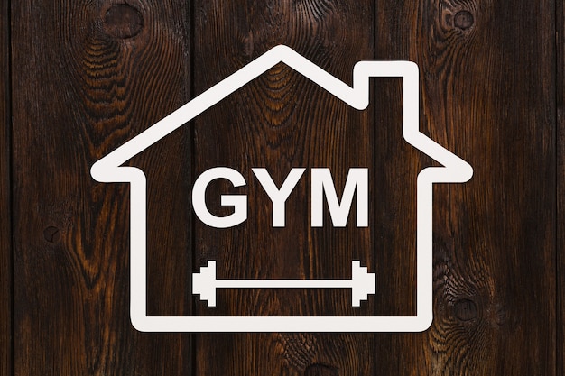 Фото Бумажный дом с текстом gym внутри на деревянном фоне. абстрактное спортивное концептуальное изображение