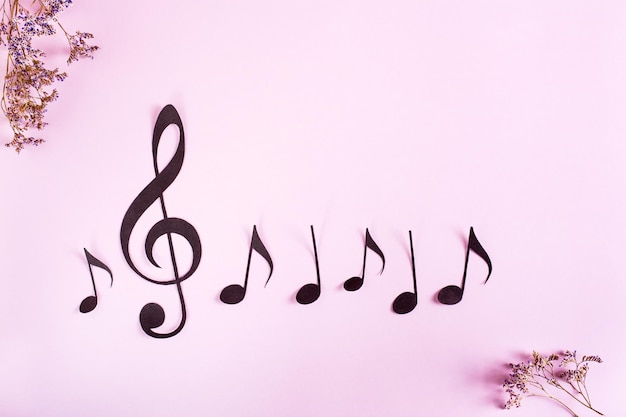 Paper musical clef and notes in a row and dried flowers on a pink background Top view