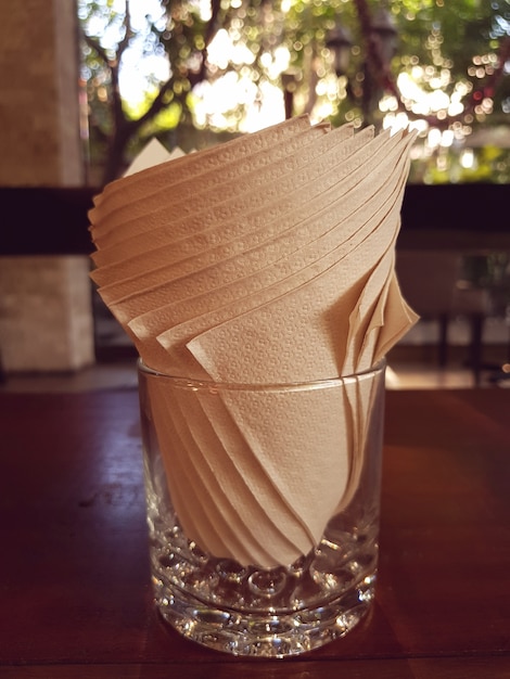 Paper napkins placed in drinking glass on wooden table at the restaurant